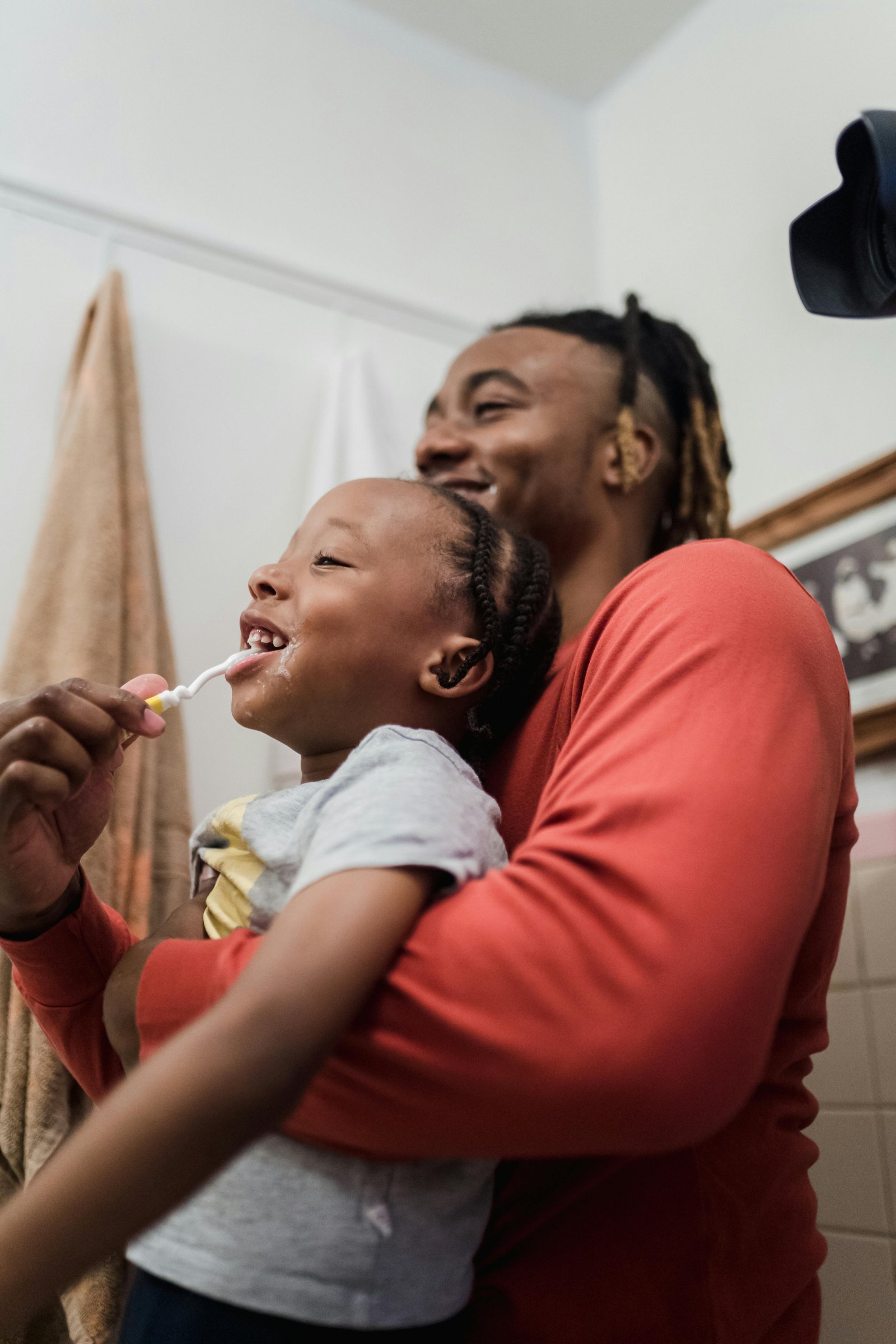 A father holds his child while helping them brush their teeth