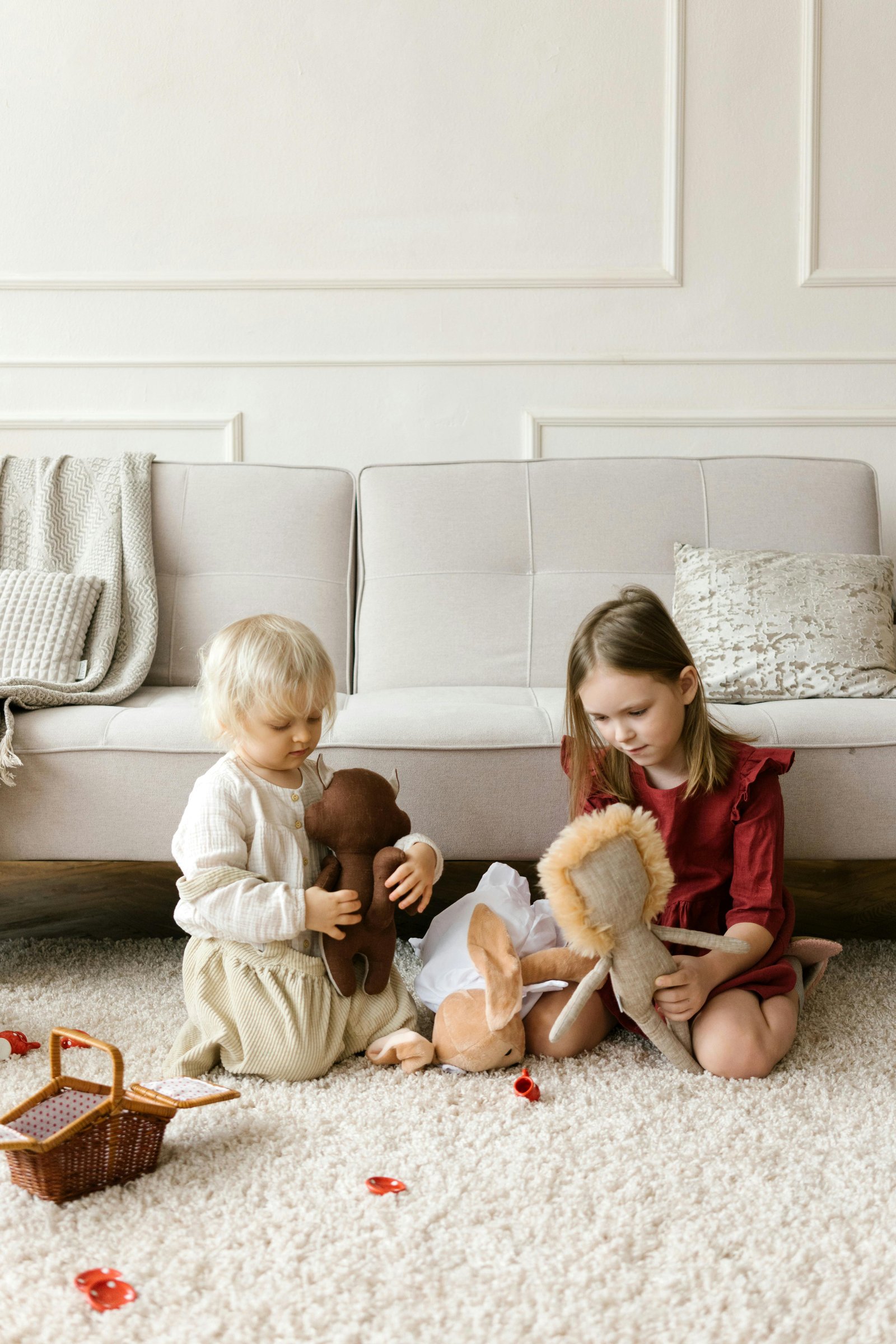 Two children play with stuffed animals on the carpet