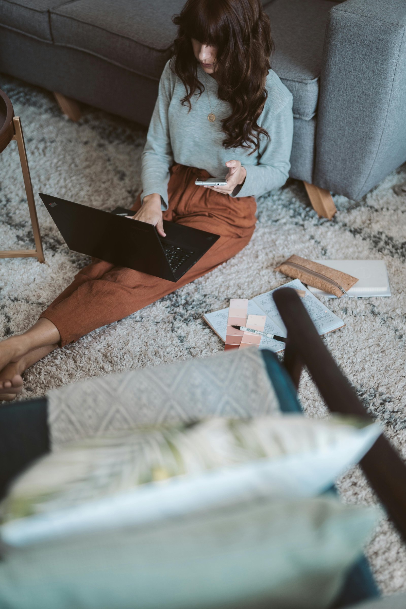 Woman sits on floor texting while on her computer